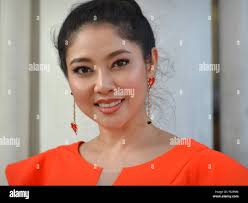 Giovane donna tailandese con begli occhi indossa un moderno abito arancione  e pone per la fotocamera al fine di mostrare il suo perfetto trucco degli  occhi Foto stock