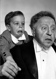 Plano medio de Arthur Rubinstein con John Rubinstein a hombros posando  haciendo una mueca.