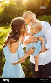 Little cute baby girl with mom and dad, beautiful daughter sitting on  strong fathers arms and smile to caring mother, happy young family at the  park Stock Photo - Alamy