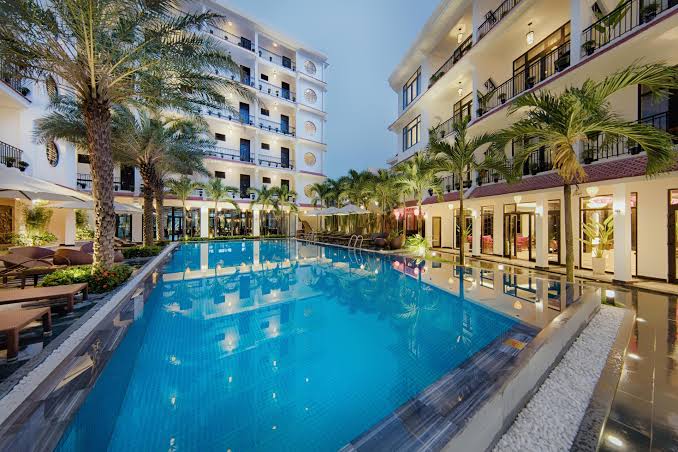 Hồ bơi ngoài trời nằm giữa khuôn viên resort, được bao quanh bởi hàng cây nhiệt đới và các dãy phòng có ban công riêng.