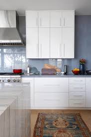The coastal theme is highlighted by the distressed beige rug and the medium tone wooden floor; Blue Kitchen Cabinetry With Gray Marble Transitional Kitchen