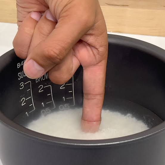 Close up POV shot of measuring water level over rice inside a rice cooker pot inner scale markings visible