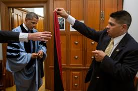 Valet Paul Reyna, right, and Trip Director Marvin Nicholson assist  President Barack Obama with his academic regalia