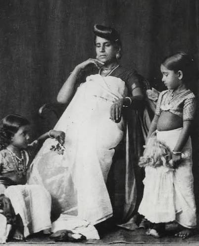 Queen Sethu Lakshmi Bayi (standing) and her younger sister (on the floor). Both the sisters were adopted into the House of Travancore, as the royal family had no female heir. The involvement