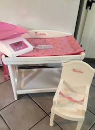A wooden changing table with a heart cutout, rounded legs, and storage space (just like the real thing!) a soft reversible changing pad to keep bitty baby comfortable; This Is An American Girl Doll Itty Bitty Baby Said It Is A Nursery It Has The Changing Table A High Chair A American Girl Baby Doll Bitty Baby Itty Bitty
