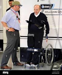 British Sir Frank Williams (R), Managing Director and Team Principal of  Williams team chats standing with an unidentified person inside his team's  garage before the first practice session at Marina Bay Street