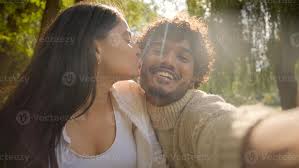Smiling multiracial couple Indian girlfriend female girl Indian Arabian  male boyfriend boy recording blog woman man enjoy date make selfie photo  kiss gesture talk call family park outdoors 49976434 Stock Photo at
