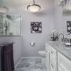 White and lavender bathroom features lavender walls framing inset framed medicine cabinet over white washstand topped with white marble countertop next to window covered in lavender roman shade over white tiled floor accented with gray border tiles. 1
