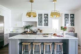 Behind the island, a stainless steel cooktop is fixed between. White And Gray Kitchen With Gold Pendants And Dip Dyed Counter Stools Contemporary Kitchen