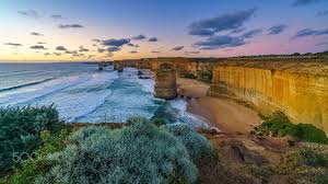 Couple walking past the 12 apostles, great ocean road, victoria, australia discover see the towering 12 apostles, get up close to native wildlife, and take in iconic surf breaks, pristine rainforest and misty waterfalls along the spectacular great ocean road. Twelve Apostles At Sunset Great Ocean Road At Port Campbell Australia Twelve Apostles Marine National Marine National Park Twelve Apostles Places To Travel