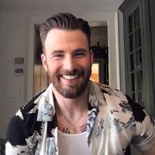 Chris Evans in floral print over a tank top with a beaming smile and the  chest tattoos generously peeking out? To quote Gaga: “We are soaking wet.”