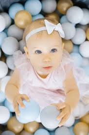 Una niña de un año está dientes ella roe un juguete de goma sentado en una  piscina con bolas de colores