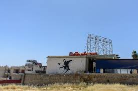 It shows a masked palestinian throwing a bouquet of flowers. Banksy In Bethlehem Banksy Street Art Bethlehem Palestine The Whole World Is A Playground