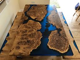 Wooden oval shaped top with epoxy resin inlay sitting on a cedar stump. Resin River Dining Table Rooso Designs