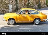 Young man driving yellow vintage Fiat 850 Sport Coupe ...