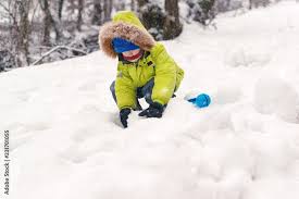 Happy child in warm clothing playing with snow. Child in warm clothing in  winter. Kid making snowballs on winter cold day. Child playing with snowball  maker. Winter fun outdoors. Winter holidays. Stock