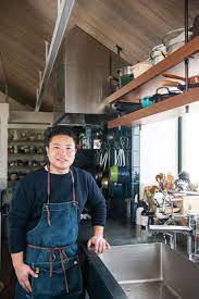 自宅キッチンに立つ栗原心平さん 洗い物がたまってもジャブジャブ洗える広いシンクがいい と特注した モノは多くても 調理スペースはしっかりと確保 撮影 写真部 岸本絢 キッチン 吊り棚 キッチン 日本のキッチン