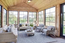 A cozy small sunroom with wicker chairs and a foldable table, with lots of blooms in pots and roman shades. 21 Beautiful And Inspiring Farmhouse Sunroom Decorating Ideas
