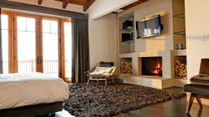 Interior of a large modern bedroom with a rock wall feature fireplace, brown walls, ceiling fan and red and white furnished bed. 17 Impressive Master Bedrooms With Fireplaces