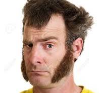 A Man With Large Sideburns Looks At The Camera With One ...