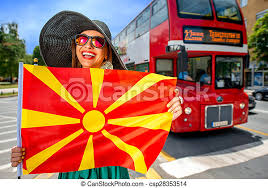Displays a stylized yellow sun on a red background, with eight rays extending from the center to each edge. Woman With Macedonian Flag In Skopje City With Red Routemaster Bus On Background Promoting Tourism In Macedonia Canstock