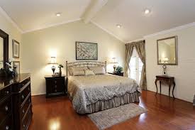 A very attractive primary bedroom featuring gray walls and vaulted ceiling lighted by a glamorous chandelier. Vaulted Ceiling Lighting Bedroom Swasstech