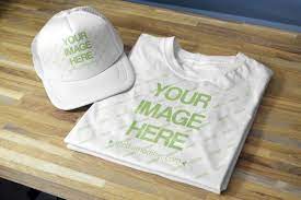 A Double Mockup For Showcasing Your Shirt And Cap Hat Designs A Folded T Shirt And A Blank Snapback Hat Lying On A Folding T Shirts Caps Hats Clothing Mockup