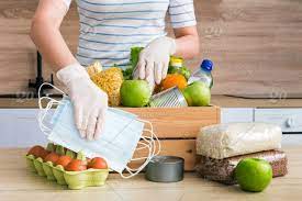 If we think of it, if each of the. A Girl In Medical Gloves Dial Charity Donation Crate Box With Food Oil Water Herbs Apples And Fruits Cereals And Canned Food Rice Pasta Medical Masks White Wooden Kitchen Background Close Up