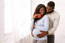 Lovely Afro Couple Cuddling At Home Next To Window, Pregnant Wife Eating  Apple, Husband Hugging Her Belly, Copy Space Stock Photo, Picture And  Royalty Free Image. Image 134768457.