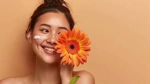 Young Asian woman smiling touching shoulder holding gerbera flower brown  background