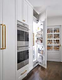 Kitchen features creamy white cabinets fitted with a white paneled beverage fridge with pull out wine trays paired with carrera marble countertops and a glazed white subway tiled backsplash. Hidden Refrigerator Design Ideas