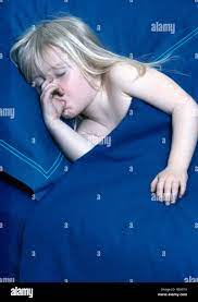 Small blonde girl sucking her thumb and sleeping in bed with blue duvet and  pillow Stock Photo - Alamy