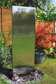 Water trickles from the top of the mirror onto the bed of rocks to mimic the sounds of a waterfall, adding ambiance to your living room, office, or hallway H130cm Vertical Stainless Steel Water Wall With Plastic Reservoir By Ambiente 429 99