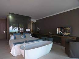 Camera da letto moderno bianco con vasca da bagno e grande letto grigio accanto a vegetali frondosi nel piatto sulla parte superiore del pavimento di legno il rendering 3d foto stock. Vasca In Camera Tutto Quello Che Devi Sapere Se La Desideri
