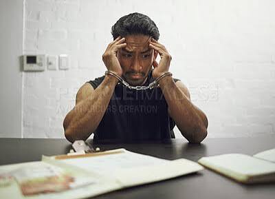 Man, criminal and handcuffs in fear for interrogation, drugs or crime in  arrest on table in room. Worried male person, gangster or suspect in jail,  justice or guilty fraud, theft or illegal