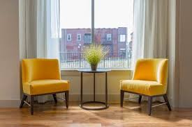 Two Yellow Chairs Flank Table With Plant In Front Of Window Looking Out At Red Building Easy Home Decor Living Room Without Sofa Home Decor