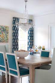Chic dining room features creamy beige paint on upper walls and wainscoting on lower walls fitted with windows dressed in white roman shades accented with black greek key ribbon trim surrounding a round wood and marble dining table lined with black and white bone inlay dining chairs, made goods ines chairs, illuminated by a turquoise blue beaded sphere pendant, currey & co alberto orb chandelier. French Turquoise Velvet Dining Chairs Contemporary Dining Room