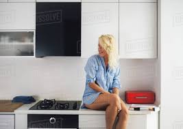 He sat down at the counter of the diner and ordered a cup of coffee. Woman Sitting On Kitchen Counter Stock Photo Dissolve