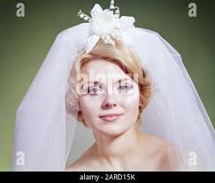 1960 BIONDA DONNA SPOSA INDOSSARE MERLETTO SPOSA NET VELO TENUTA ROSSO E  BIANCO BOUQUET DI FRONTE A VETRATE COLORATE