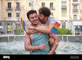 Gay man biting his boyfriends ear while hugging and laughing holding LGBT  flags Stock Photo - Alamy