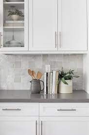 Beautiful ivory & gray kitchen design with ivory kitchen cabinets & kitchen island with gray quartz countertops, sink in kitchen island, subway tiles backsplash and restoration hardware clemson pendants. Light Gray Glazed Backsplash Tiles With Gray Quartz Countertop Transitional Kitchen
