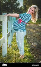 A blonde, cute, pregnant girl standing in the late evening sun next to a  white wooden fence Stock Photo - Alamy