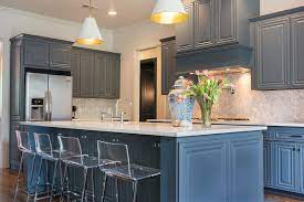 Glass front blue cabinets mounted against gray marble tiles with brass edging flank stacked blond wood floating shelves. Marble Chevron Kitchen Backsplash Transitional Kitchen