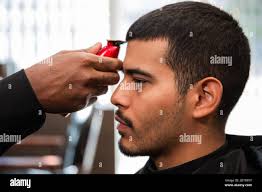 Un barbiere afroamericano taglia e rasa i capelli di un uomo latino  ispanico con un pizzetto e baffi con un rasoio elettrico in un barbiere  Foto stock