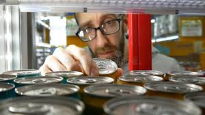 Close-up of the Hand of a Bearded Man with Glasses Taking One Can of Soda  or Energy Drink in a Store Fridge Stock Photo