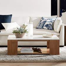 A white waterfall coffee table sits on gray teak pavers poolside flanked by restoration hardware aegean teak chairs accented with white cushions and a black end table. Waterfall Coffee Table Williams Sonoma