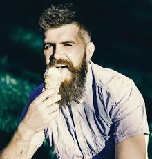 Mann med langt skjegg nyter iskrem mens han sitter på gress. Et delikat  begrep. En skjeggete mann med iskrem. Mann med skjegg og bart på opphisset  ansikt spiser iskrem, gress på bakgrunn,