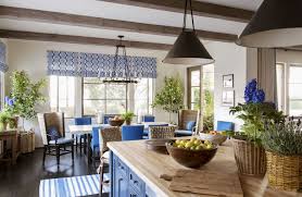 A white and blue abstract art piece hangs in a white and blue dining room from a wall clad in denim blue wallpaper and faces a white wooden dining table seating white and blue head chairs and round back blue dining chairs lit by a white ring chandelier. Blue And White Rooms Decorating With Blue And White