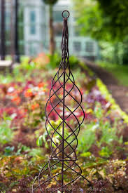 A Spiral Wrought Iron Climbing Plant Support Adds A Formal Note To A Garden Bed Iron Plant Garden Patio Furniture Garden Obelisk Metal