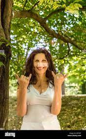 Close up of busty classy mature woman smiling at the camera while doing  welcome shaka sign against green garden background with copy space Stock  Photo - Alamy